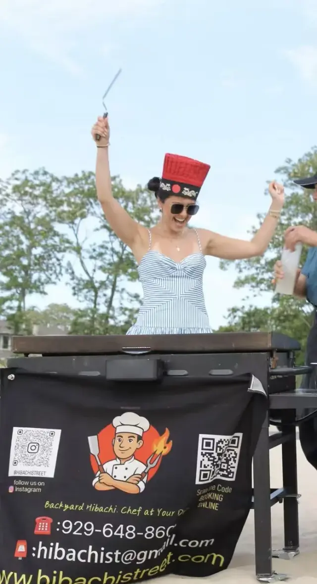 Party guest cheering in a flaming chef hat during a hibachi show