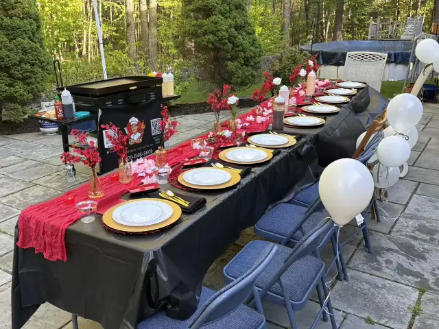 Red and black hibachi party table setup with gold plates and balloons